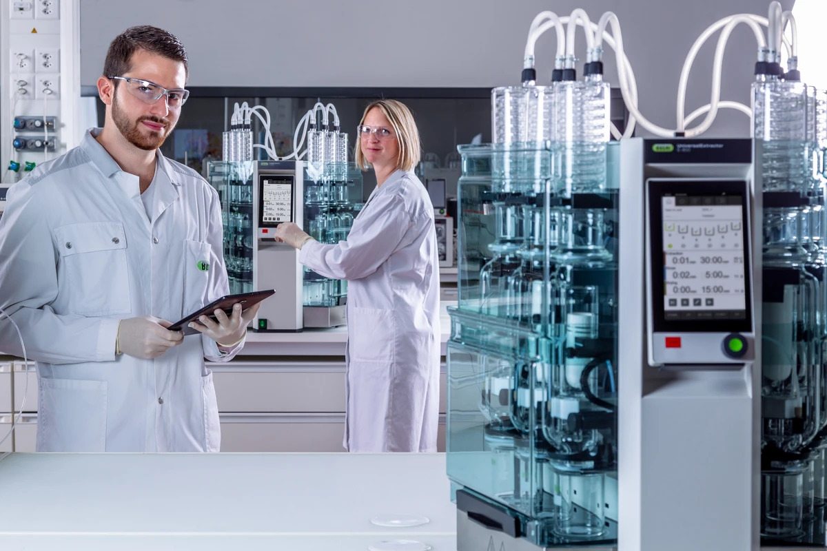 Dos técnicos de laboratorio junto a extractores BÜCHI E-800 que procesan varias muestras en paralelo